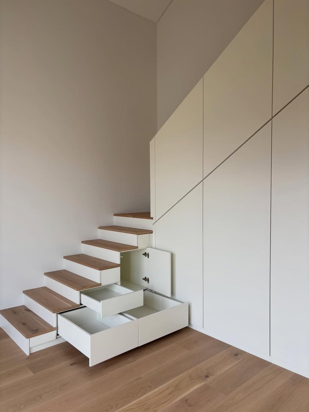 Treppe mit geöffneten Schubladen und einer Klappe in den Stufen, daneben die weiße Schrankwand