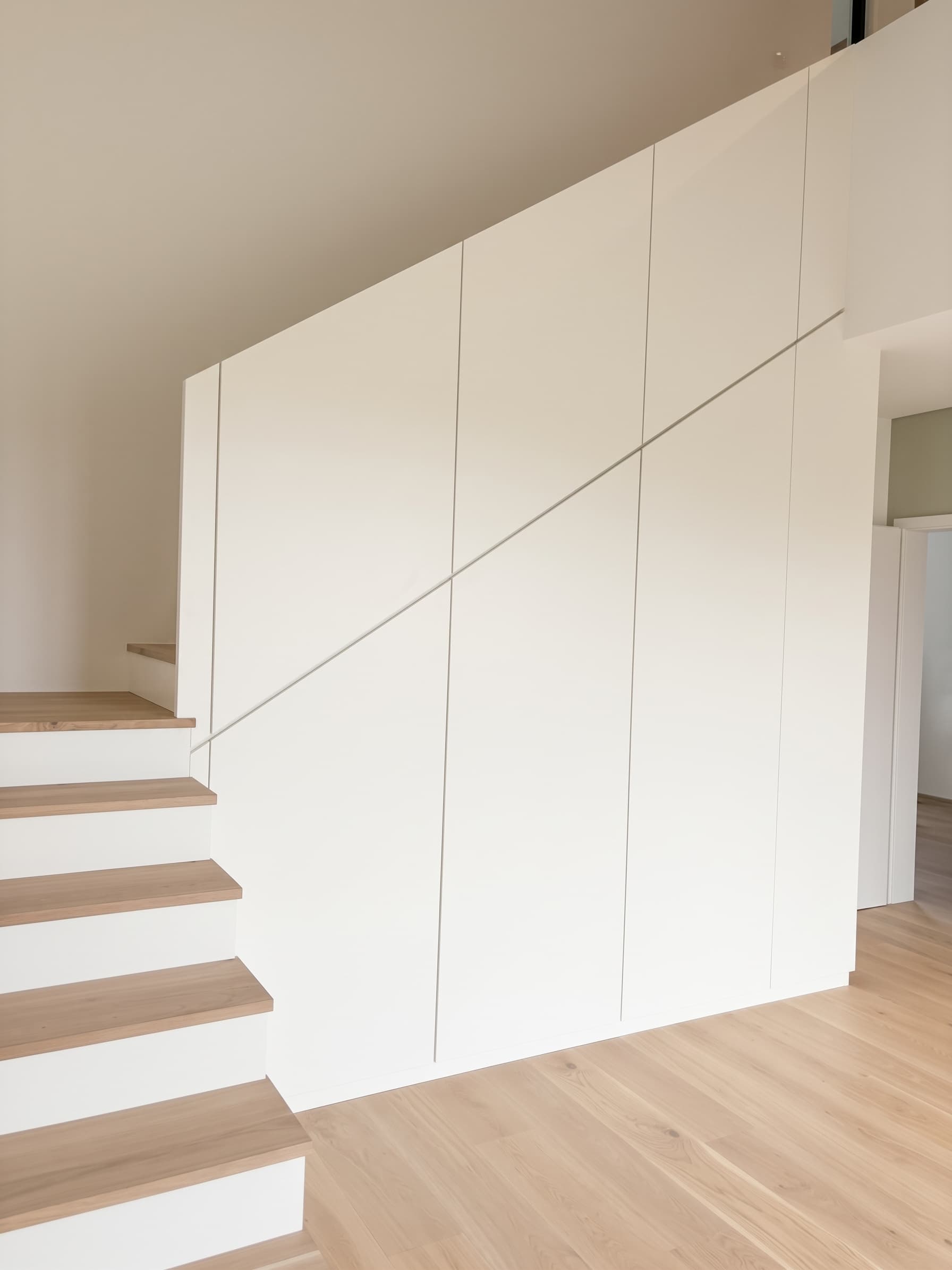 Weiße, grifflose Schrankwand entlang einer Treppe mit Eichenstufen, gebaut von der Holzwerkstatt Deliu